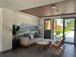 Un vestíbulo moderno con sofá, mesa de centro y sillones, un gran cuadro abstracto en la pared y una señal de salida.