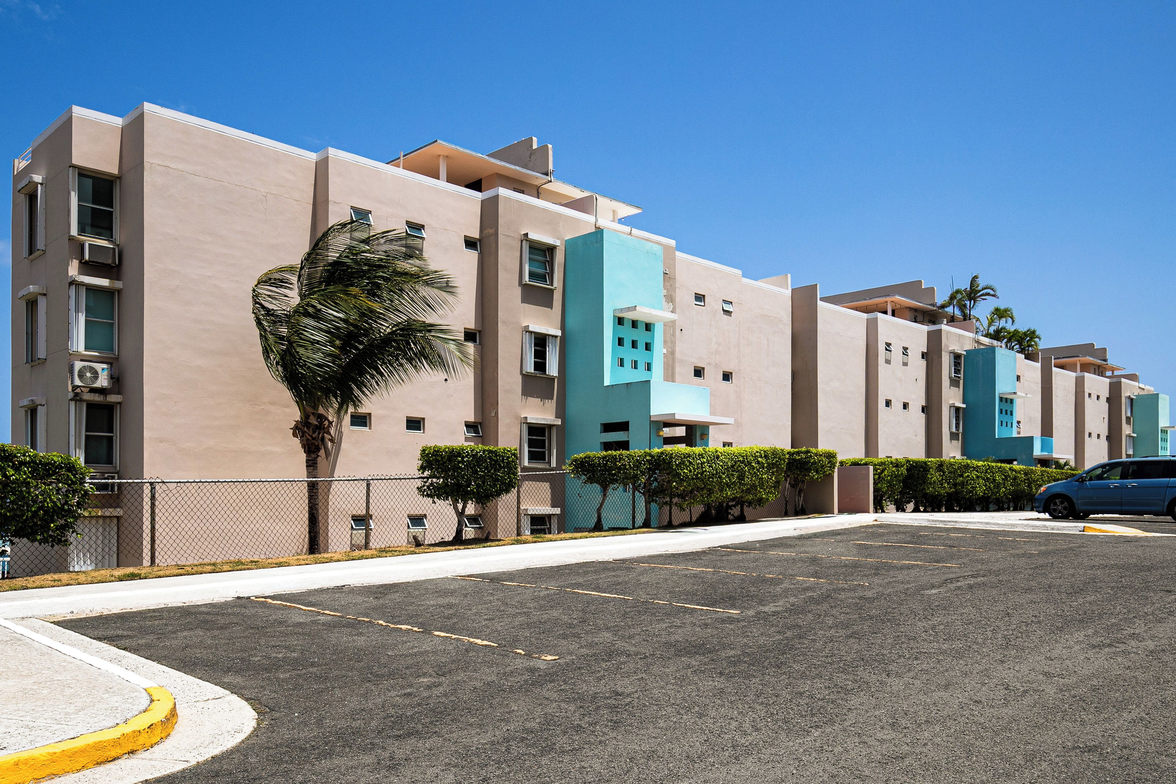 A multi-story hotel with a modern design, featuring balconies and a parking area.