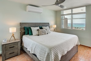 A bedroom with a bed, nightstands, a ceiling fan, an air conditioner, a window with a view, and a lamp. - Walk to the Beach! Quiet Resort Retreat in Maunabo (Maunabo)