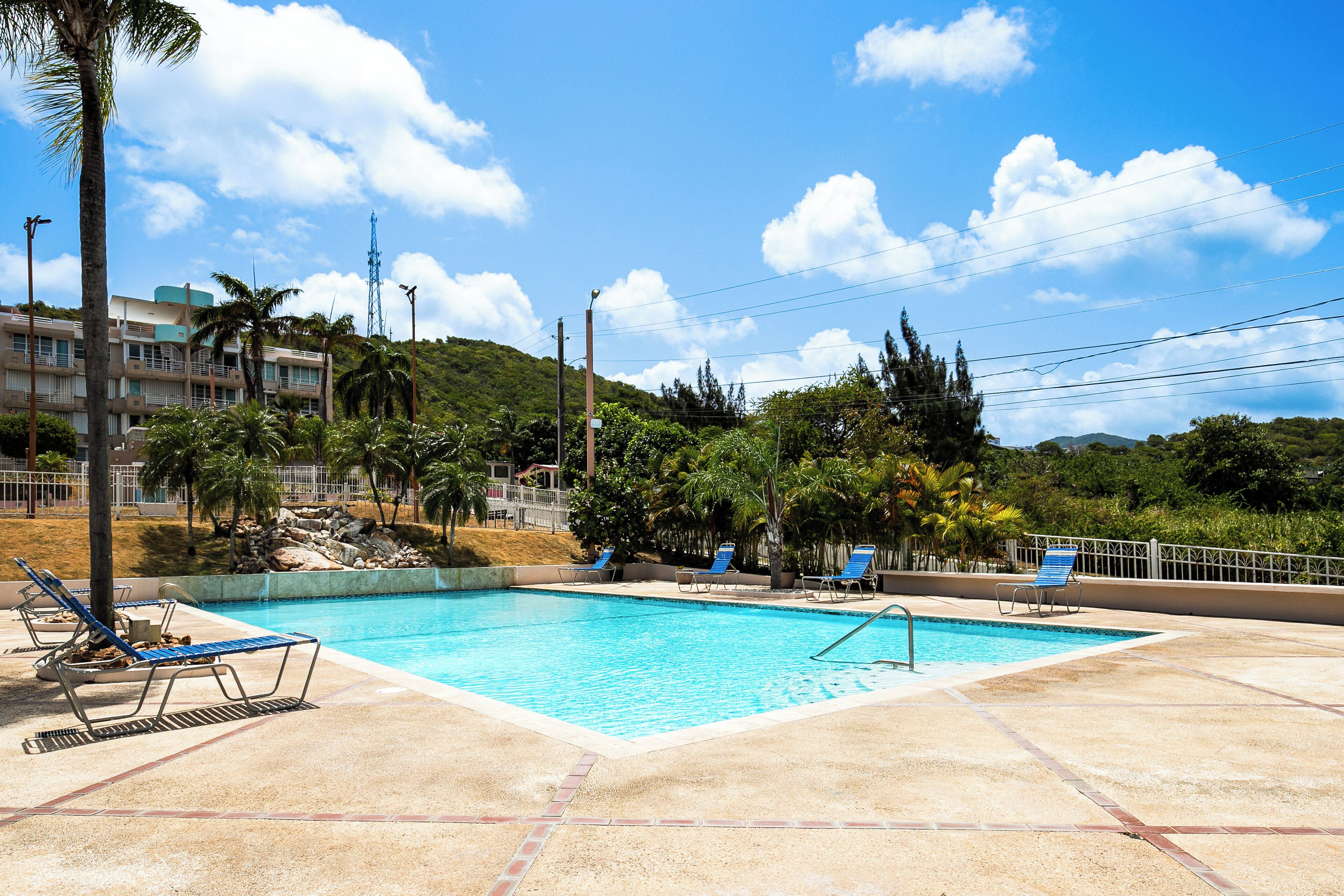 Una piscina con sillas de descanso, rodeada de palmeras y un paisaje montañoso.