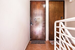 Eine Holztür mit Metallbeschlägen und Schlüsselloch, ein weißes Metallgitter und ein gefliester Boden.