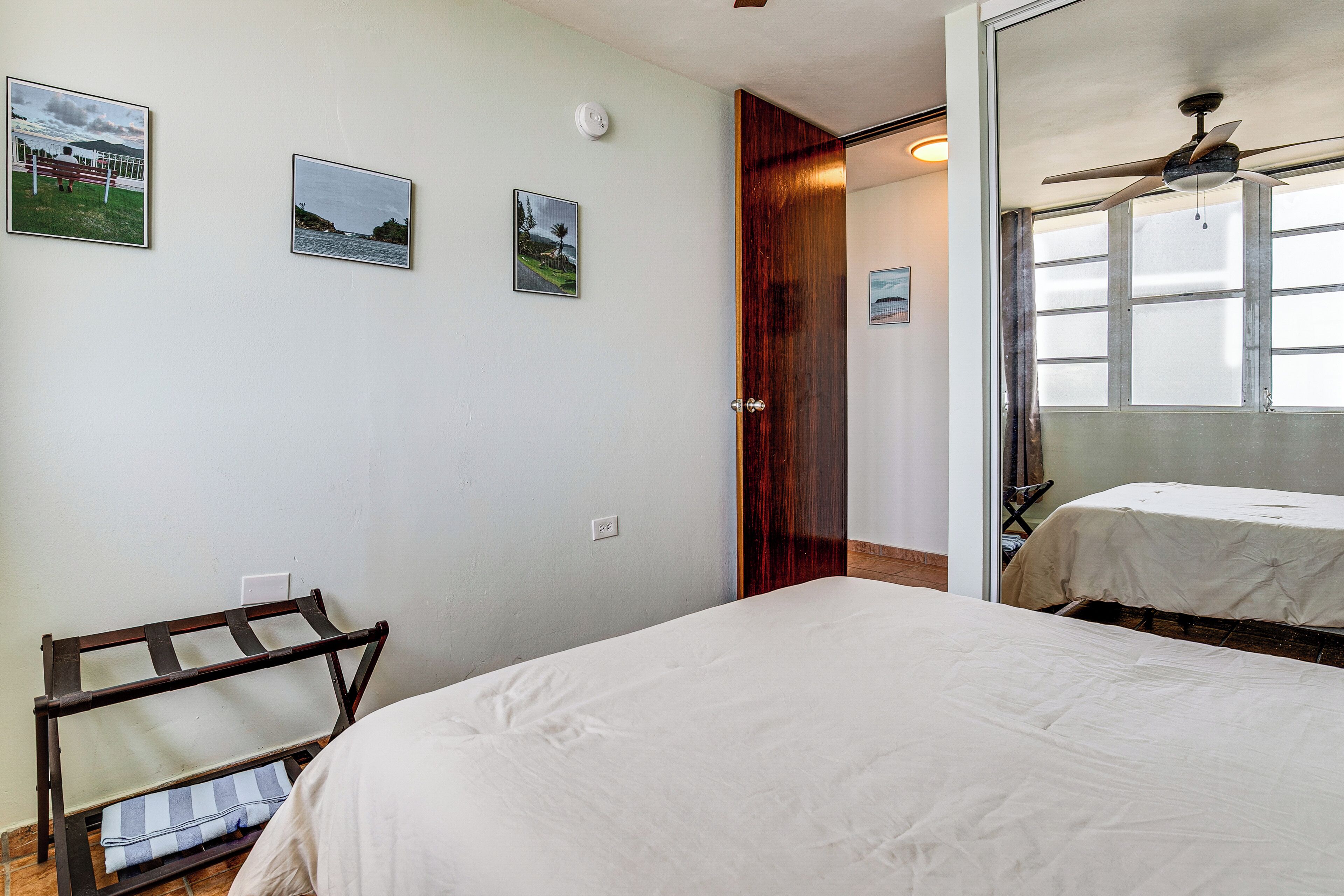 A bedroom with a bed, a wooden bench, a door, and a window with a ceiling fan.