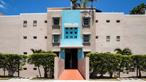 A building with a central blue section, multiple windows, and a red pathway leading to the entrance.
