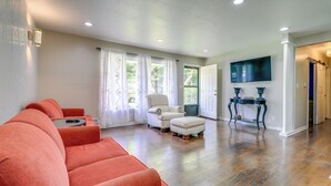 A living room with a red sofa, a white armchair, and a small ottoman. - 5 Mi to Kansas City Stadium! Bright Home w/ Yard (Kansas City)