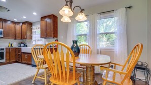 A kitchen with wooden cabinets, a dining table with chairs, and a vase on the table. - 5 Mi to Kansas City Stadium! Bright Home w/ Yard (Kansas City)
