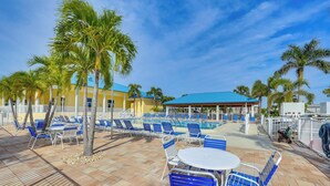 A poolside area with blue chairs, a white table, and palm trees. - Pool & Dock Access! Boater’s Base in Punta Gorda (Punta Gorda)