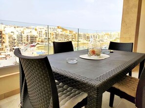 Un balcon avec une table et des chaises, un vase rempli de fleurs et une vue sur le paysage urbain.