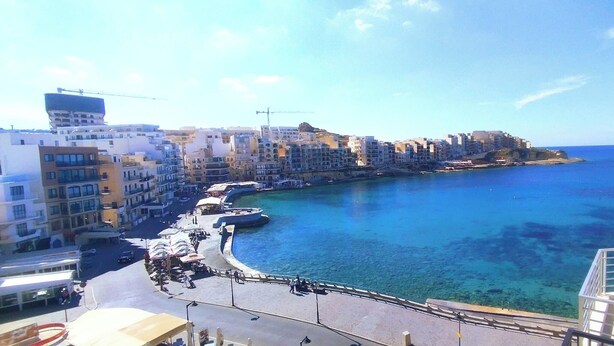 Paisatge urbà costaner amb edificis al passeig marítim, un mar blau i transparent i una zona per a vianants.