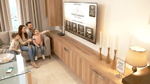 Una família en un saló modern amb una televisió de pantalla plana que mostra una interfície de smart TV, un moble de fusta i una taula de cafè de vidre.
