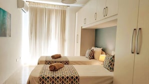 Habitació d'hotel amb dos llits, una finestra amb cortines, un ventilador de sostre i una nevera minibar.
