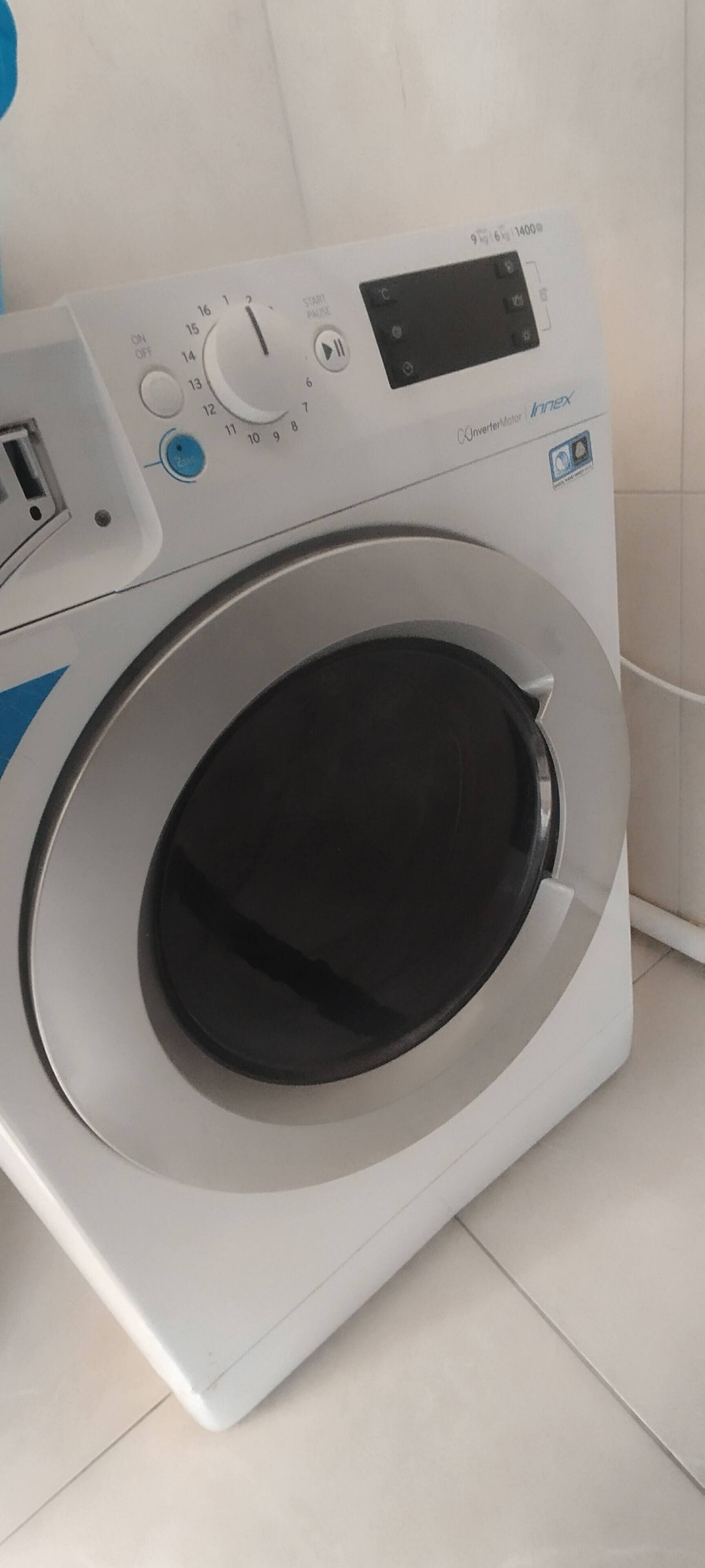 A front-loading washing machine with a digital control panel, a small display, and a blue button.