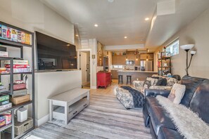 Ein modernes Wohnzimmer mit einer Couch, einem Fernseher, einem Bücherregal und einer Küche im Hintergrund.