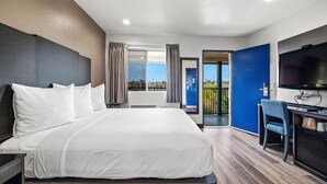 Une chambre d’hôtel avec un lit, un bureau, une chaise, une télévision et un balcon avec vue.