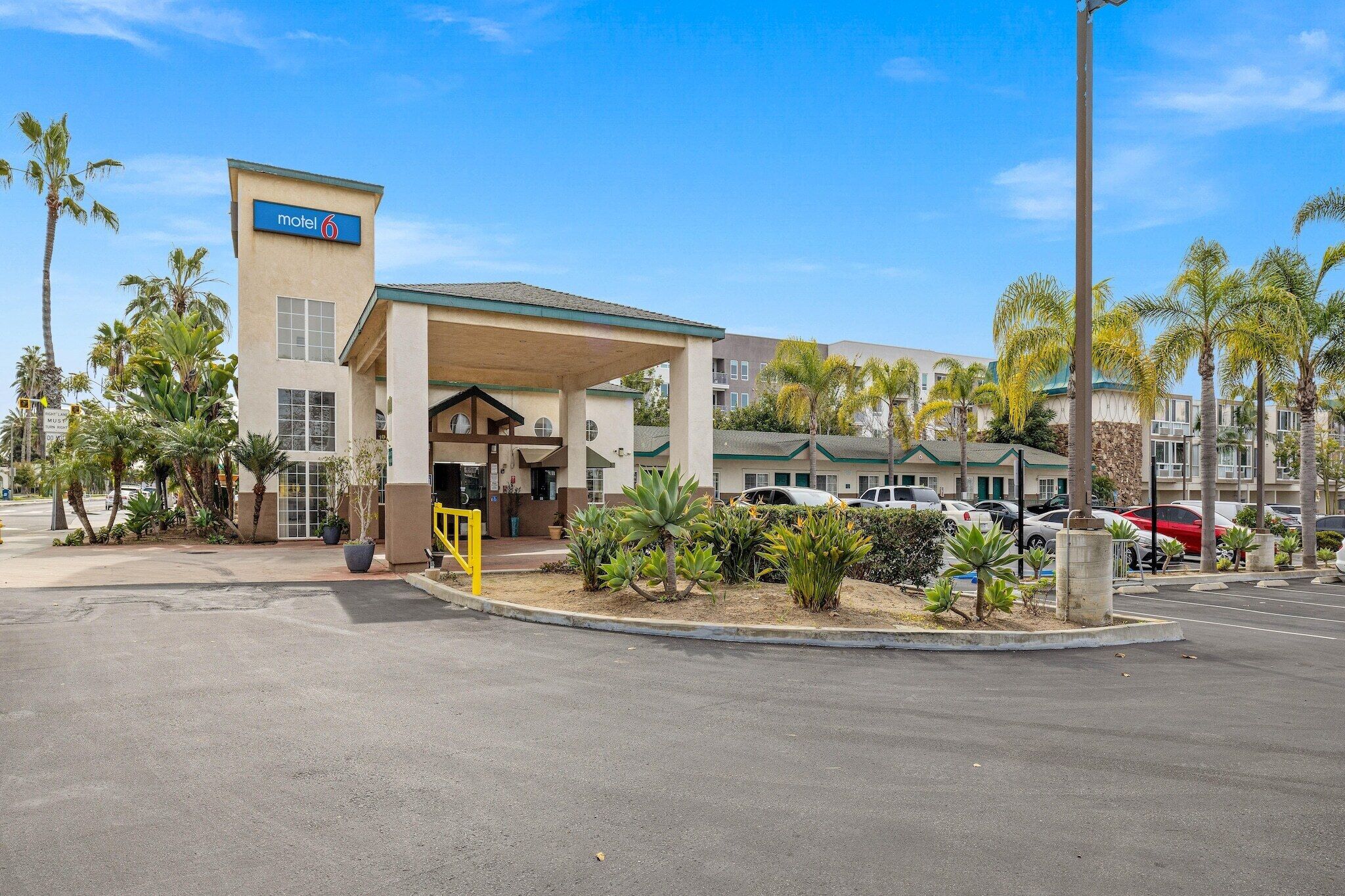 A motel with a covered entrance, palm trees, and a parking lot.