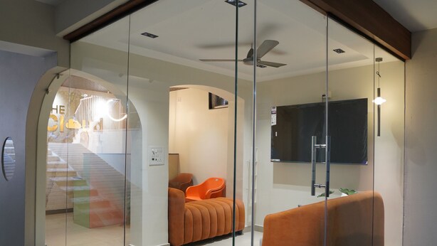 A modern interior with a glass partition, a flat-screen TV, a ceiling fan, and orange seating.