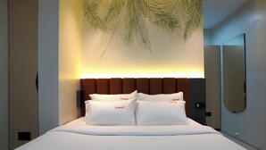 A hotel room with a bed, a headboard, a wall-mounted mirror, and a palm leaf decoration.