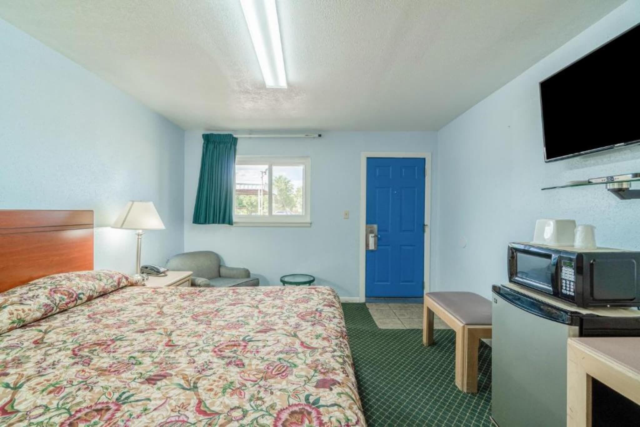 Une chambre d’hôtel avec un lit, un bureau, une chaise, une télévision, un four à micro-ondes et une porte bleue.