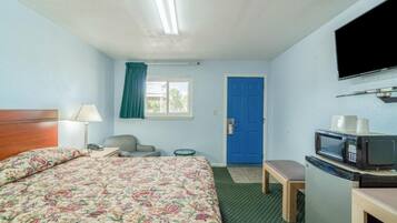 Une chambre d’hôtel avec un lit, un bureau, une chaise, une télévision, un four à micro-ondes et une porte bleue.