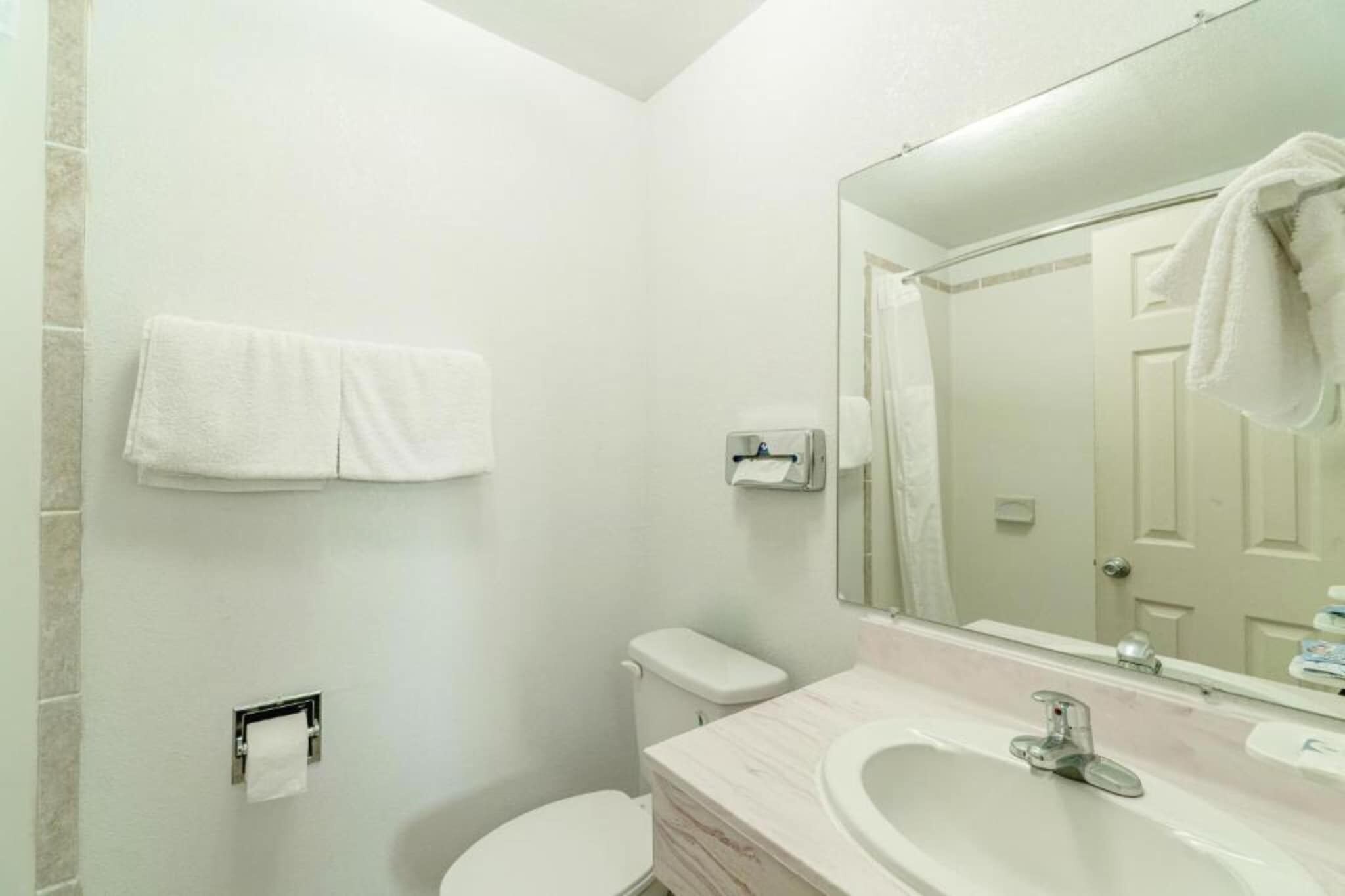 Un baño con inodoro, lavamanos, espejo y perchero para toallas.