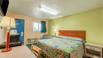 Quarto de hotel com cama, escrivaninha, cadeira, televisão e janela com cortinas.