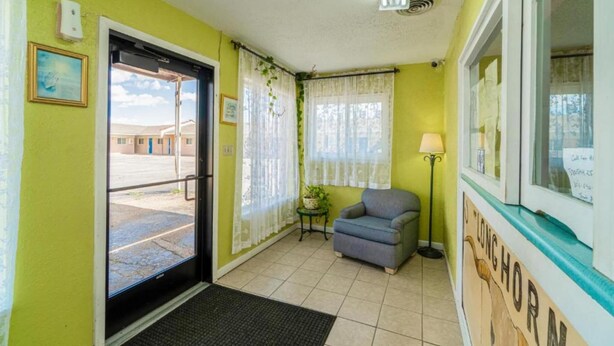 A room with a door leading outside, a small table with a plant, a lamp, and a chair.