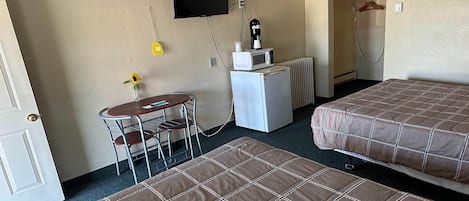 A hotel room with two beds, a small table with chairs, a TV mounted on the wall, and a shower area.