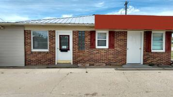 A single-story building with a brick facade, two windows with shutters, and a garage door.