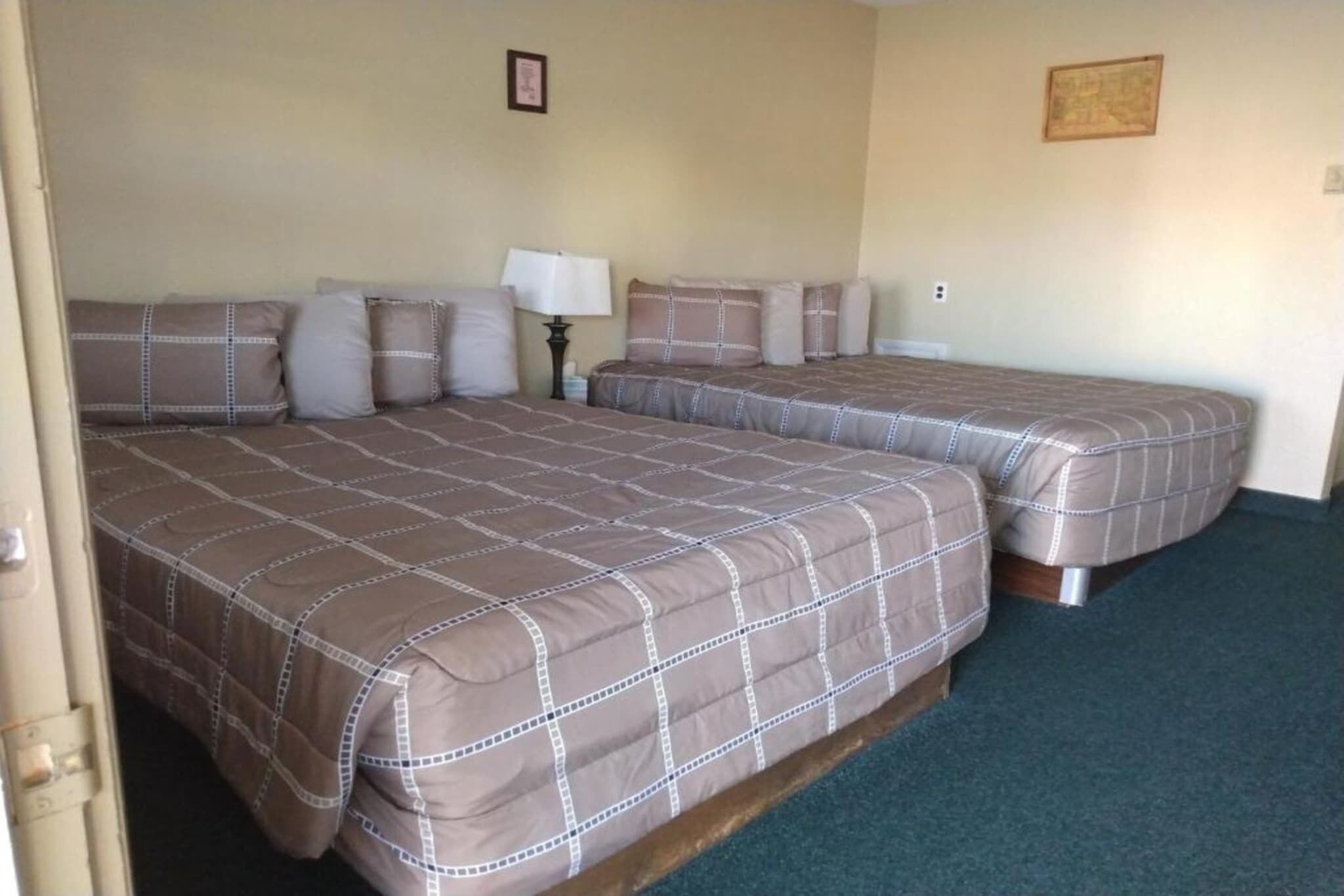 A hotel room with two beds, a nightstand, a lamp, and a framed picture on the wall.