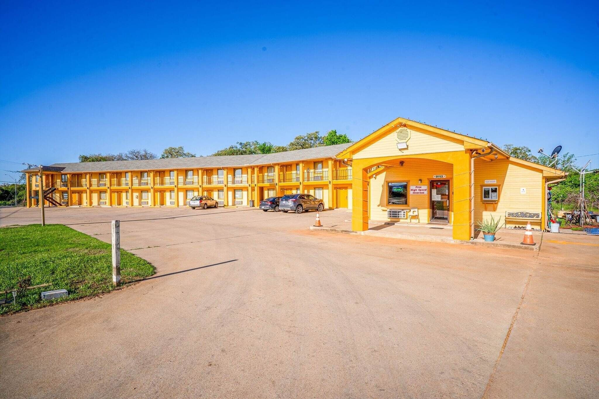 A yellow motel with a central entrance, multiple balconies, and a parking area.