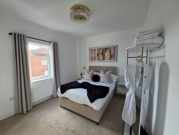 A bedroom with a bed, a hanging robe rack, a painting, and a window with curtains.