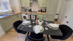 A dining table set for two with a black marble top, surrounded by black chairs, in a kitchen with light green cabinets and a window. - Newly Refurbished
Suburban Luxe By Luxe Sleep (Stockport)