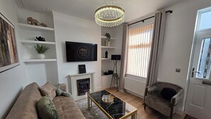 A living room with a sofa, a coffee table, a fireplace, a TV, and a chandelier. - Newly Refurbished
Suburban Luxe By Luxe Sleep (Stockport)
