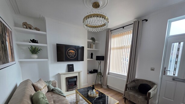 A living room with a sofa, a coffee table, a fireplace, a television, and a chandelier. - Newly Refurbished
Suburban Luxe By Luxe Sleep (Stockport)