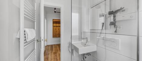 Un baño moderno con cabina de ducha de vidrio, un lavamanos blanco y una puerta de madera al fondo.