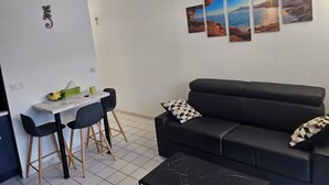 Een woonkamer met een zwarte bank, een eettafel met twee stoelen, en een wand met drie ingekaderde foto's.