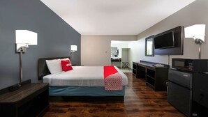 A hotel room with a bed, a desk, a television, and a refrigerator.