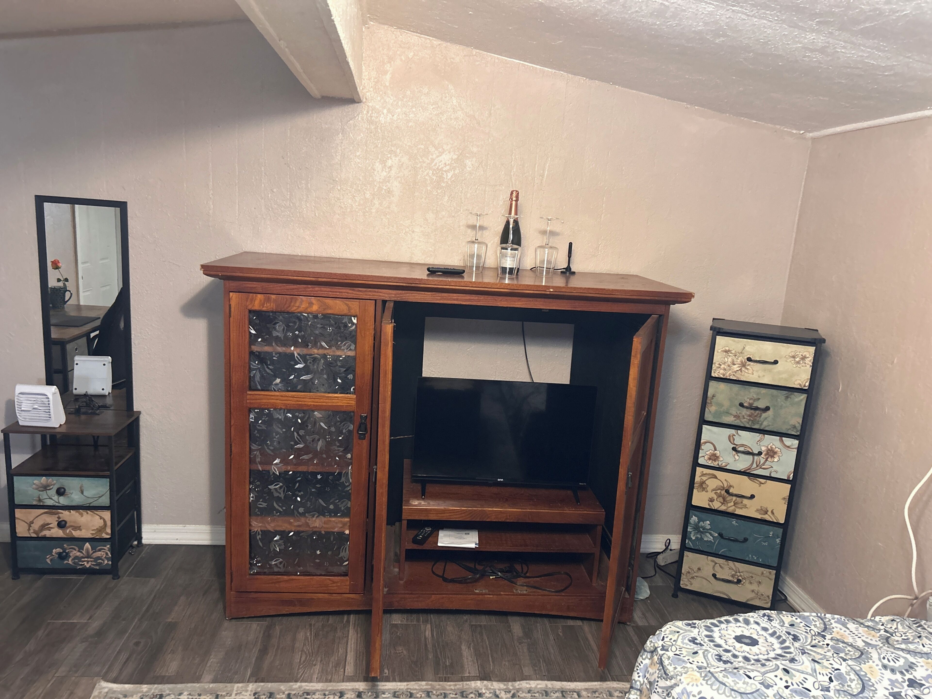 A room with a wooden cabinet with glass doors, a television on a stand, and a dresser with floral patterns.