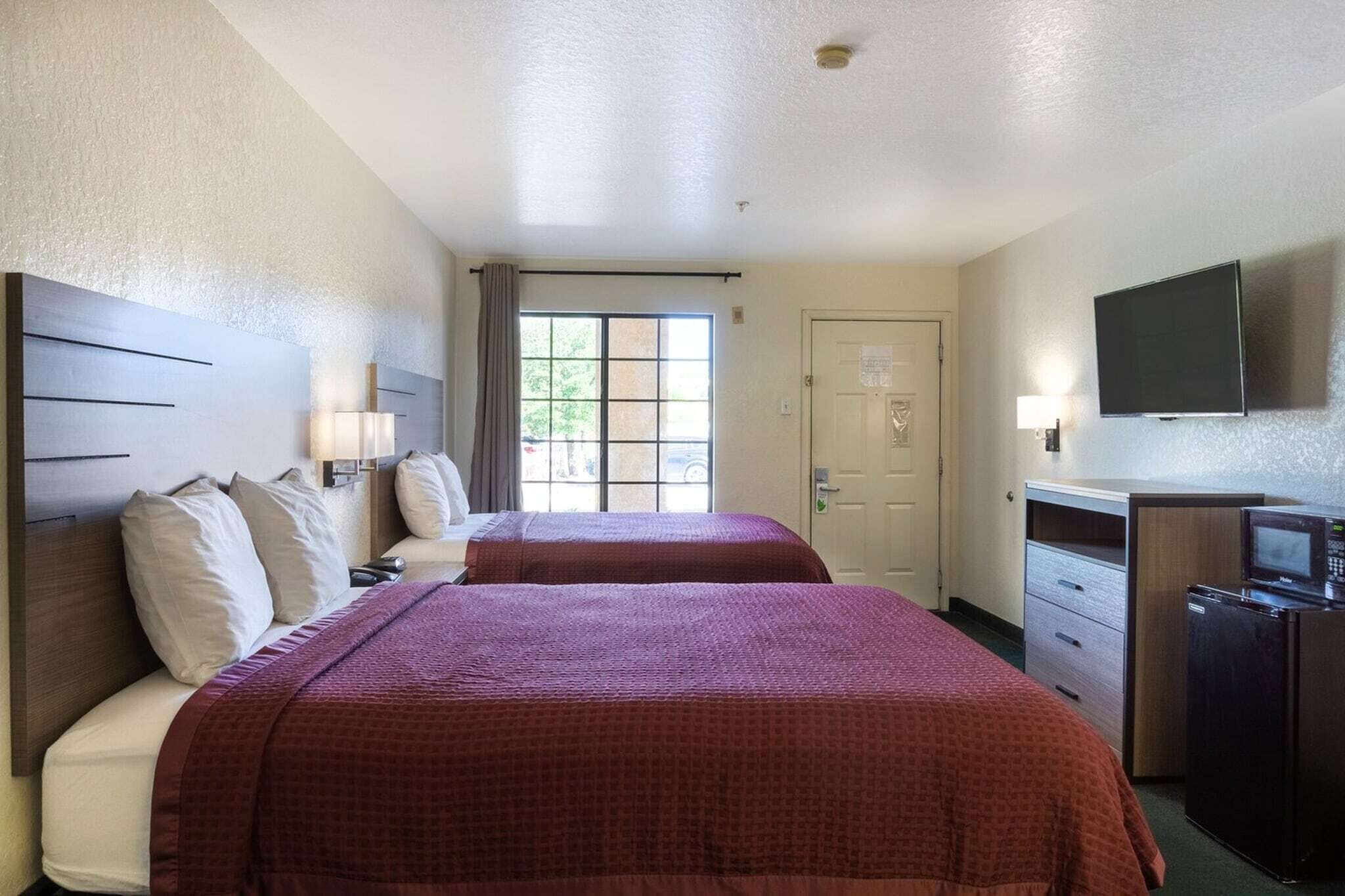 A hotel room with two beds, a television, a microwave, and a door with a window.