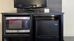 A compact kitchenette with a microwave, refrigerator, and a flat-screen TV on a stand.
