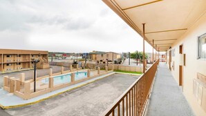 A hotel corridor with a pool area, outdoor seating, and a view of the surrounding buildings.