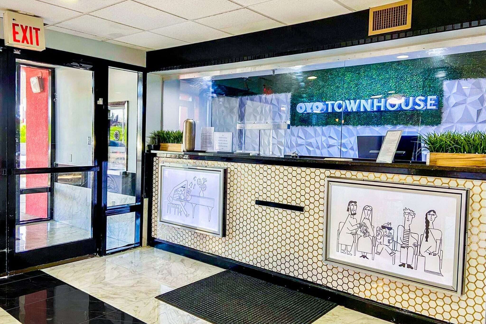 Zona de recepción con un cartel que dice 'EXIT' sobre la puerta, un mostrador de recepción y una ilustración enmarcada de una familia.