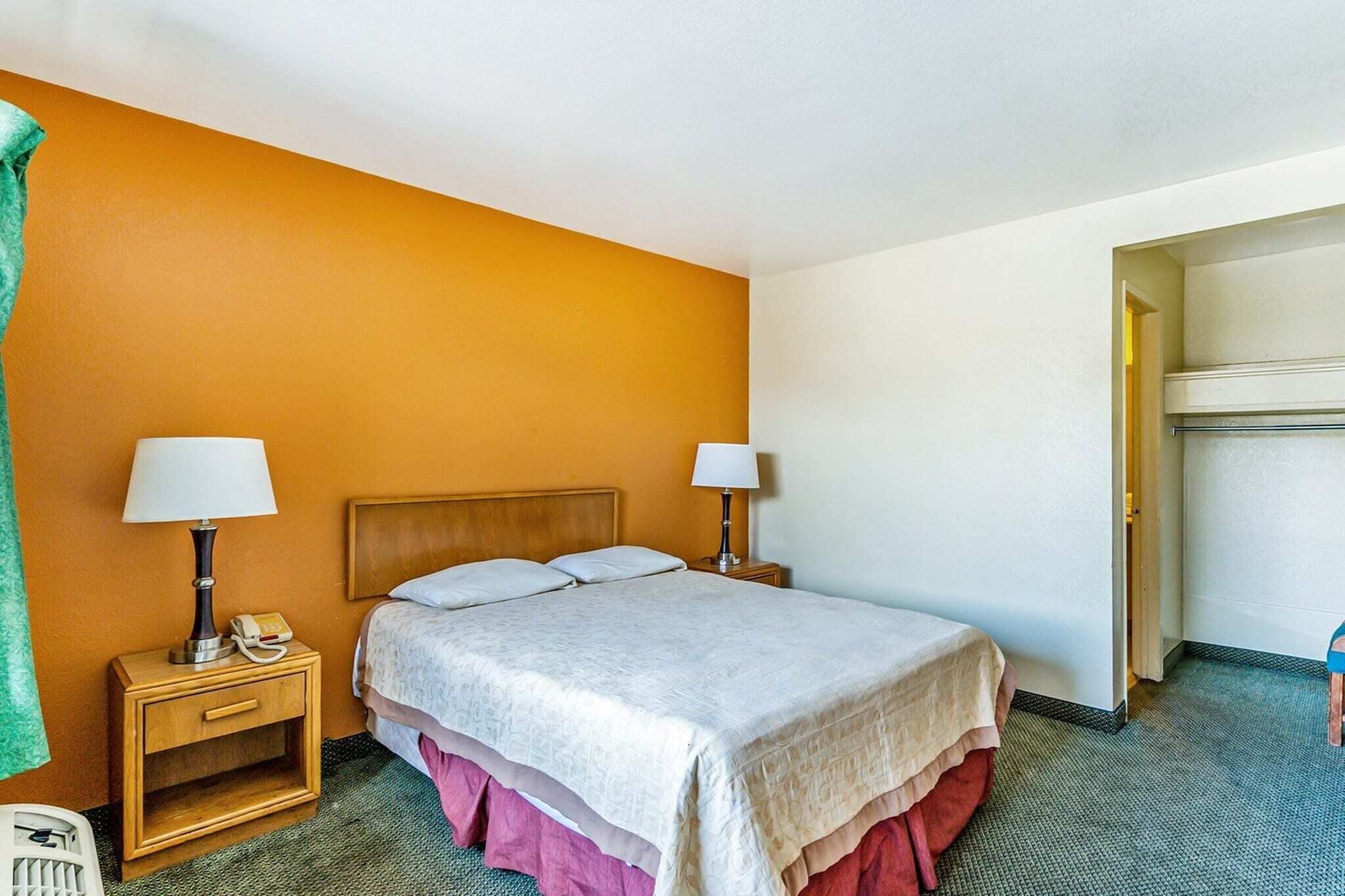 Une chambre d’hôtel avec un lit, deux tables de chevet avec des lampes, un téléphone, une serviette verte et une armoire.