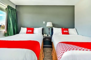 Habitación de hotel con dos camas, cada una con cubrecama rojo y blanco, una mesita de noche con lámpara y una ventana con cortinas.