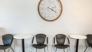 A seating area with four round tables and four chairs, a large wall clock, and a carpeted floor.