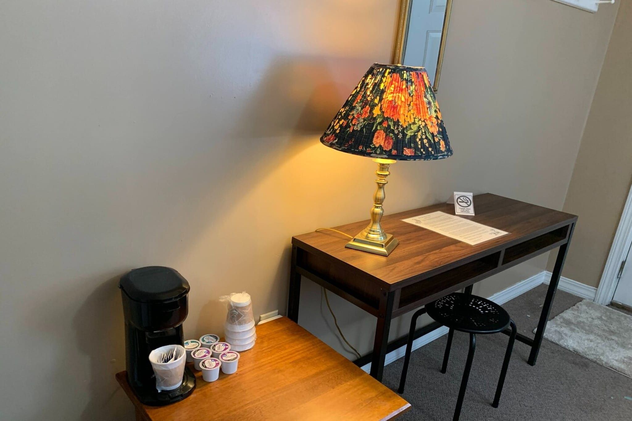 A small wooden table with a lamp, a coffee maker, and some cups.