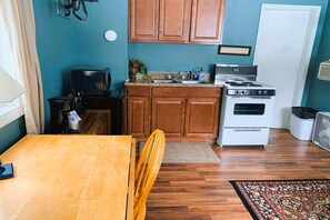 Een kleine keuken met houten kastjes, een fornuis, een spoelbak en een eethoek met een tafel en stoelen.
