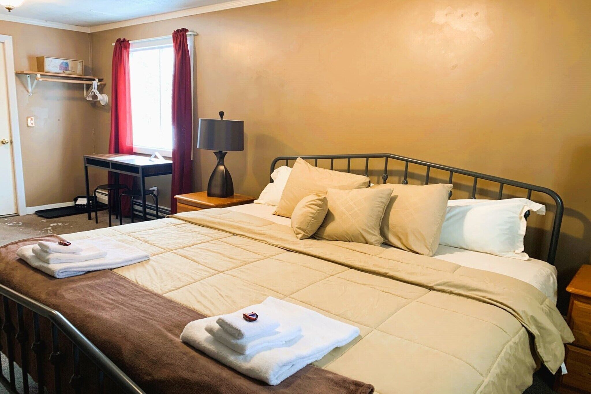 A hotel room with a bed, bedside table, lamp, desk, and window with curtains.