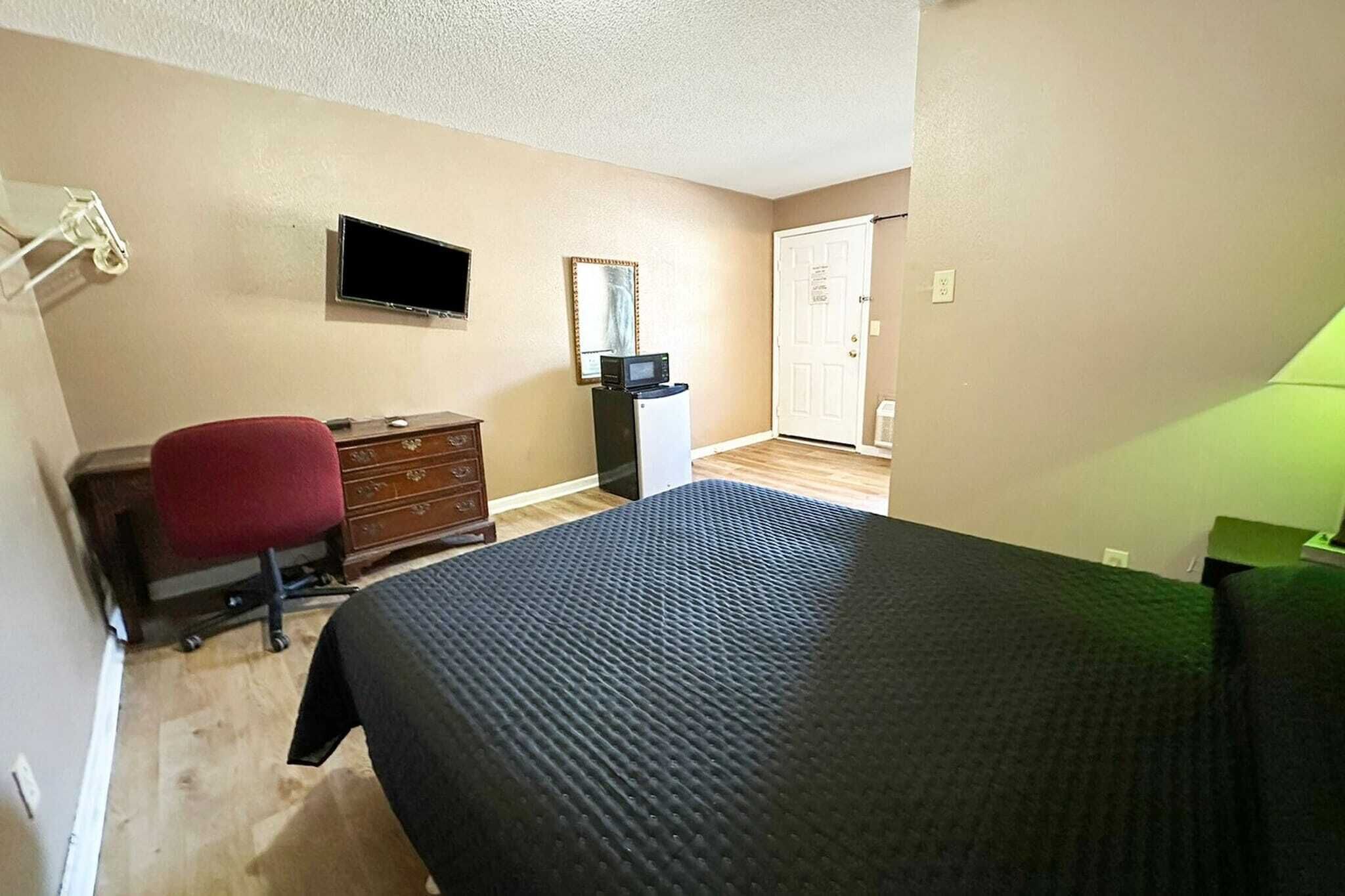Un dormitorio con cama, escritorio, silla, cómoda, televisor y puerta.