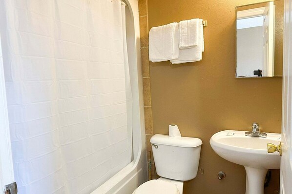 A bathroom with a white bathtub, a toilet, and a sink. - Premium Queen Bed|Sparta, GA (Sparta, GA)