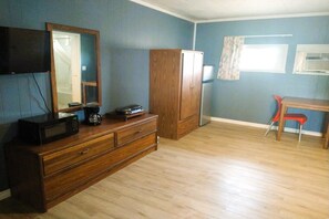 Ein Zimmer mit einem hölzernen Schminktisch, einem Flachbildfernseher, einem Kühlschrank, einem Fenster mit Vorhängen und einem roten Sessel.